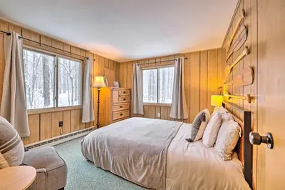 a bedroom with a bed and a chair and two windows at 1 Block to Lake Poconos Getaway with Fire Pit! in Pocono Lake
