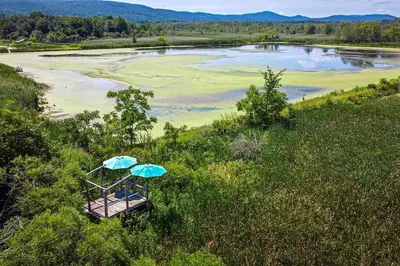 a chair with an umbrella in the grass next to a river at 1786 Farm Cottage Honeymoon Suite Renovated 2022 in Chester
