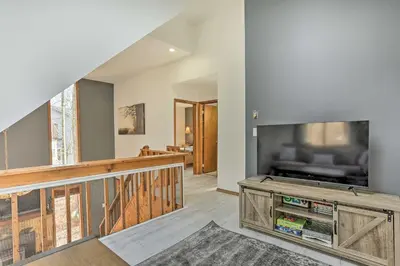 a living room with a large tv and a staircase at 4 Mi to Tubing Cozy Bushkill Cabin with Deck! in Bushkill