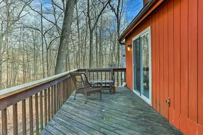 a wooden deck with a chair on the side of a red house at 4 Mi to Tubing Cozy Bushkill Cabin with Deck! in Bushkill