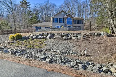 a home on a hill with a rock wall at Movie Room, Hot Tub Pocono Vacation Rental! in East Stroudsburg