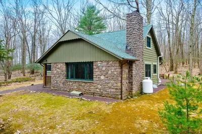 a stone house with a brick chimney on a yard at Woodland Cabin Retreat in Lake Harmony