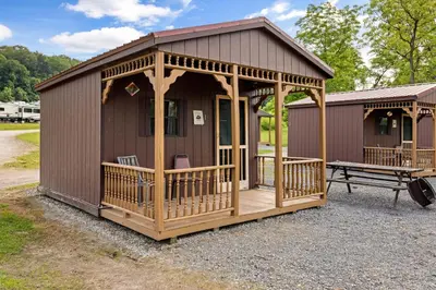 a small cabin with a porch and a bench at Cozy Cabin Within Campground in Mifflinburg
