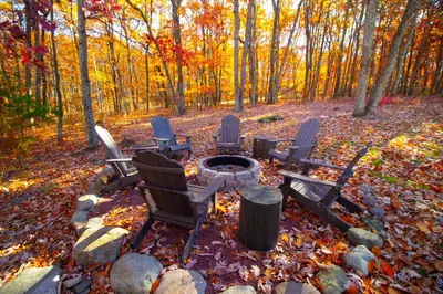 a group of chairs sitting around a fire pit in the woods at Stunning Poconos Villa- Hot Tub, Pool, Game Room, BBQ & more in East Stroudsburg