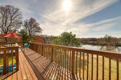 a wooden deck with an umbrella and a body of water at Dock and Fire Pit Lakefront Poconos Retreat! in Long Pond
